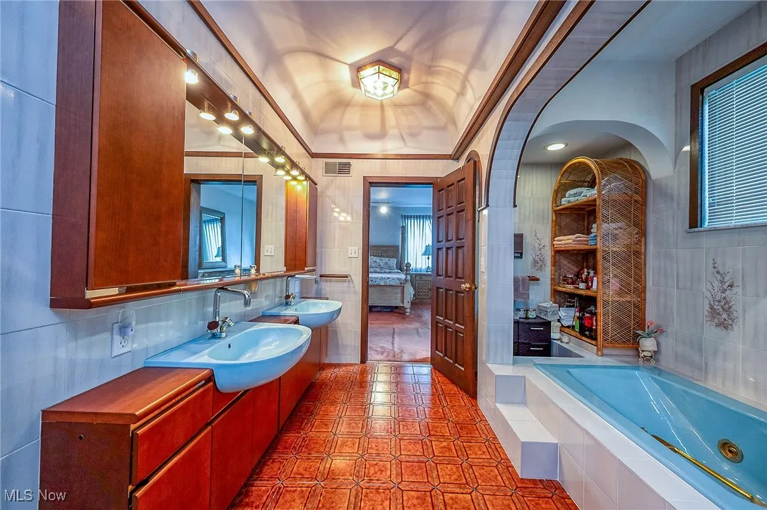 Full bathroom featuring a tub with jets, tile walls, vanity, tile patterned floors, and crown molding
