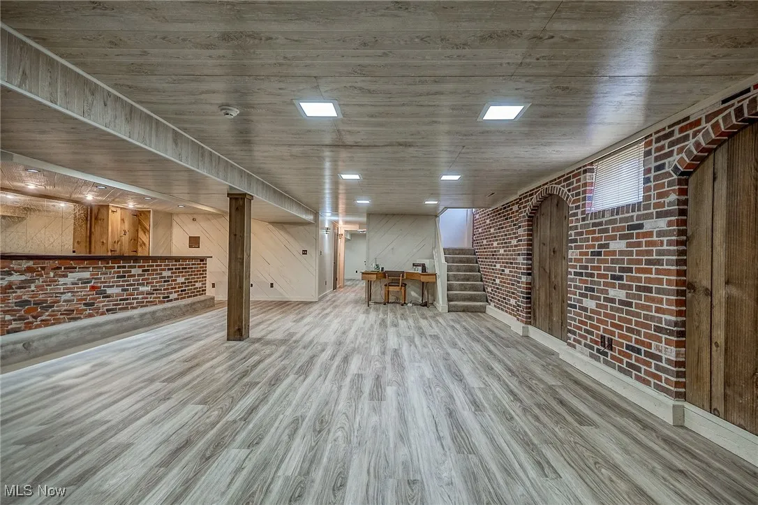 Finished basement featuring brick wall, stairs, wood finished floors, and wooden walls