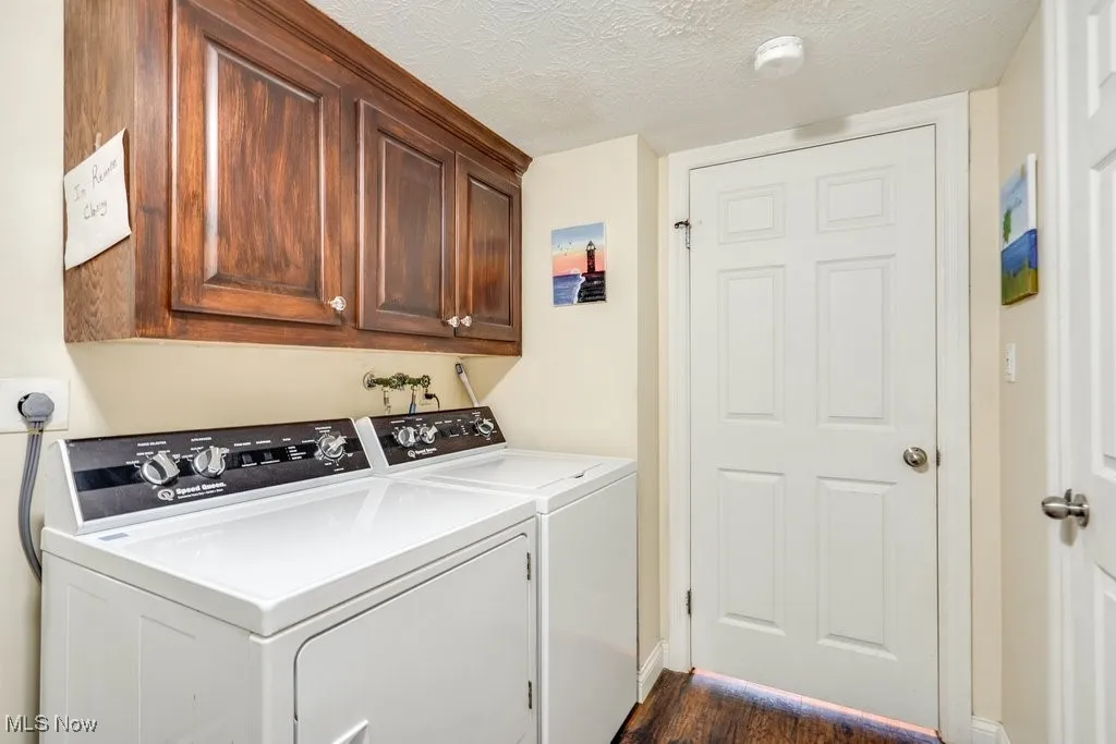 Washroom featuring washer and dryer, cabinet space, a textured ceiling, and dark wood finished floors