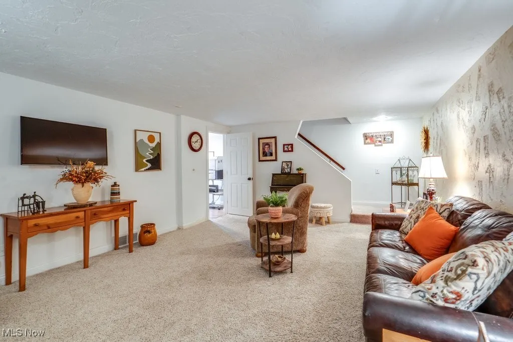 Carpeted living area with stairs and baseboards