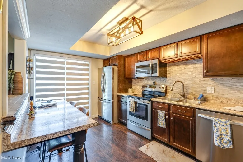 Kitchen featuring appliances with stainless steel finishes, dark wood-style flooring, tasteful backsplash, light countertops, and a textured ceiling