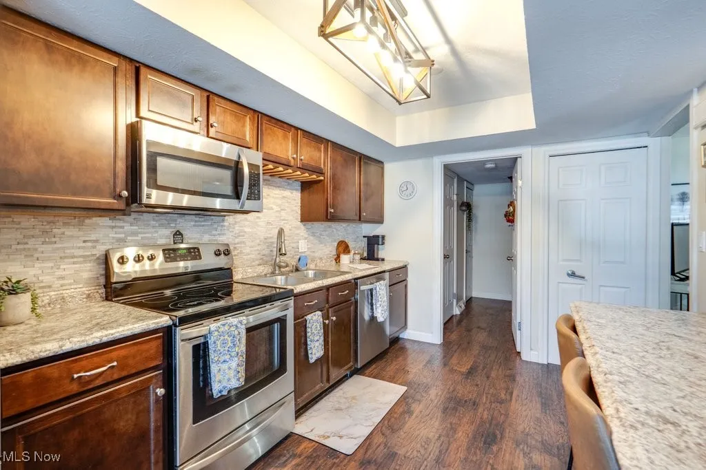Kitchen featuring stainless steel appliances, light countertops, dark wood-style floors, and tasteful backsplash