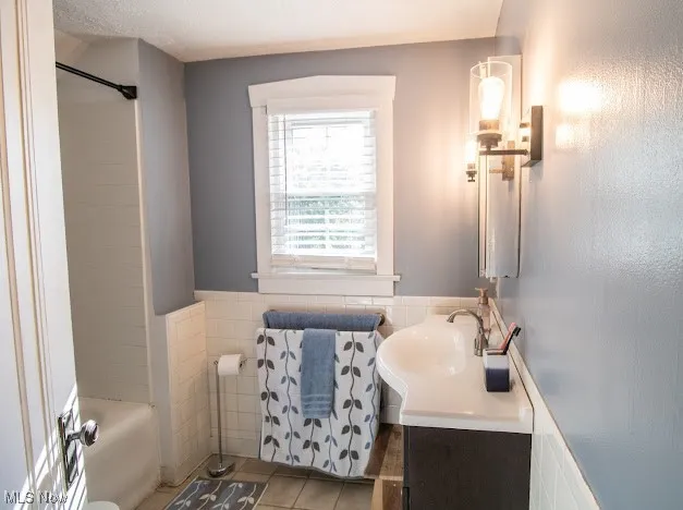 Bathroom with tile patterned flooring, vanity, tile walls, and wainscoting