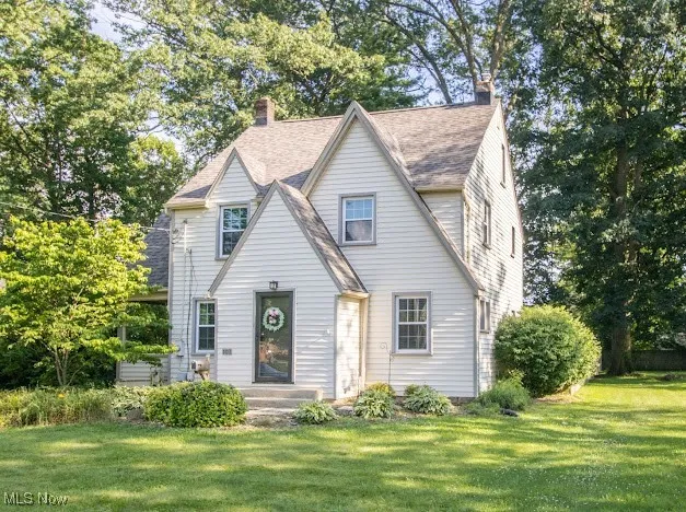 View of front of home with a front yard, a chimney, and a shingled roof