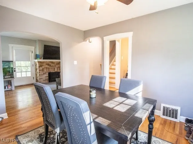 Dining room with arched walkways, stairs, a fireplace, wood finished floors, and a ceiling fan