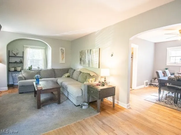 Living room featuring arched walkways, light wood-style floors, and ceiling fan