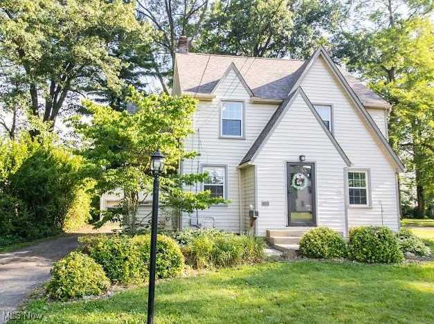 View of front of property featuring a front yard, a chimney, and roof with shingles