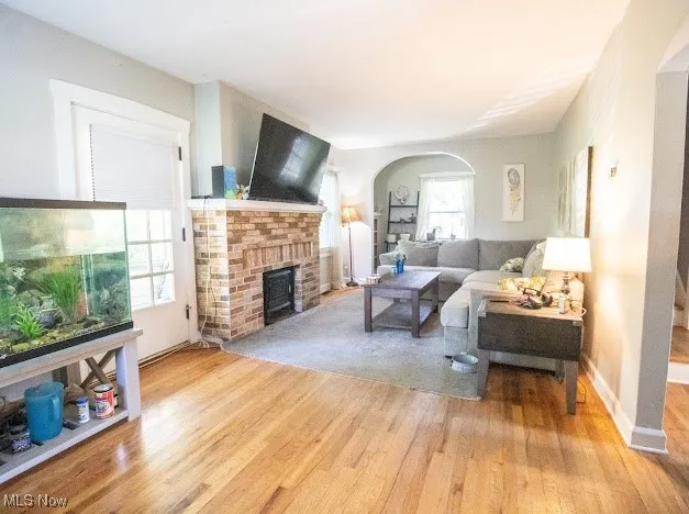 Living area with arched walkways, a brick fireplace, and light wood-style flooring