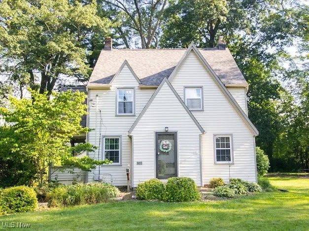 View of front of property with a front lawn, a chimney, and a shingled roof
