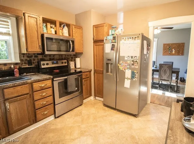Kitchen featuring appliances with stainless steel finishes, dark countertops, a ceiling fan, tasteful backsplash, and brown cabinets