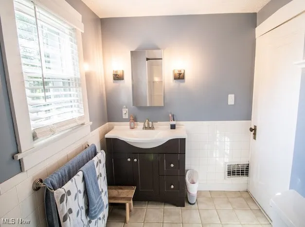 Bathroom featuring tile walls, vanity, tile patterned flooring, and a wainscoted wall