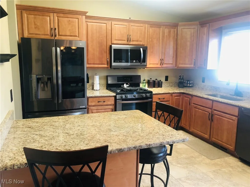 Kitchen with appliances with stainless steel finishes, a breakfast bar, a sink, light stone counters, and brown cabinets