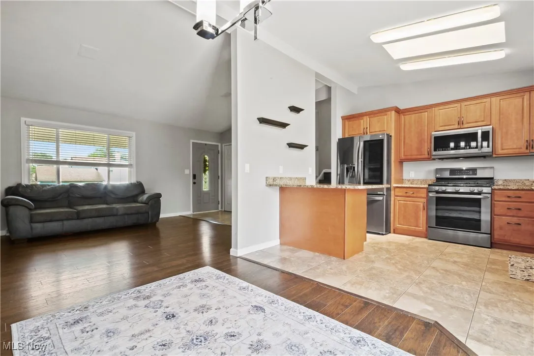 Kitchen featuring stainless steel appliances, open floor plan, light stone countertops, light wood finished floors, and high vaulted ceiling