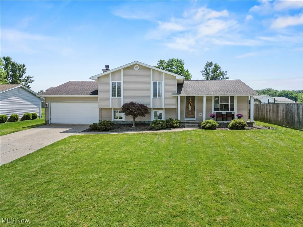 Split level home with covered porch, a garage, driveway, and roof with shingles