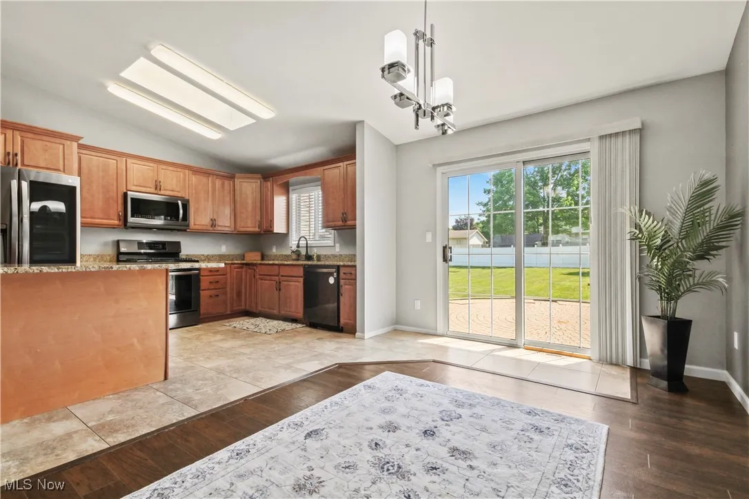 Kitchen featuring appliances with stainless steel finishes, vaulted ceiling, healthy amount of natural light, light stone counters, and brown cabinets