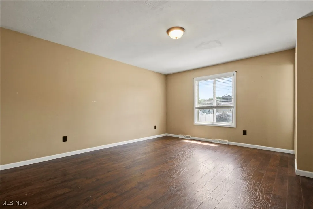 Spare room featuring dark wood-style floors and baseboards