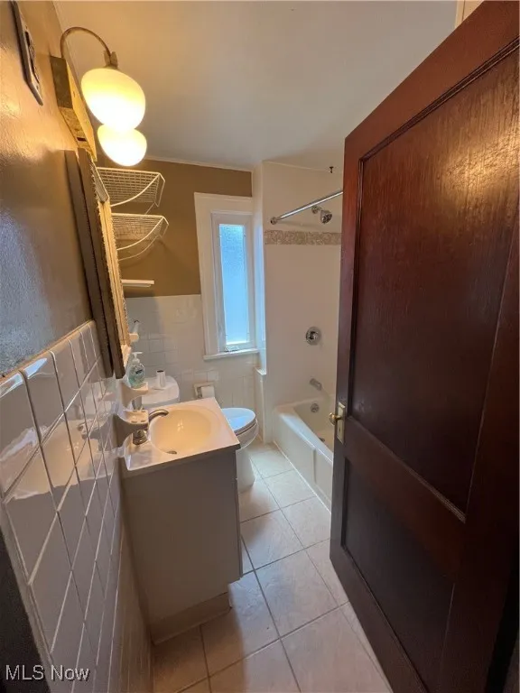Full bathroom with tile patterned floors, shower / tub combination, vanity, wainscoting, and tile walls