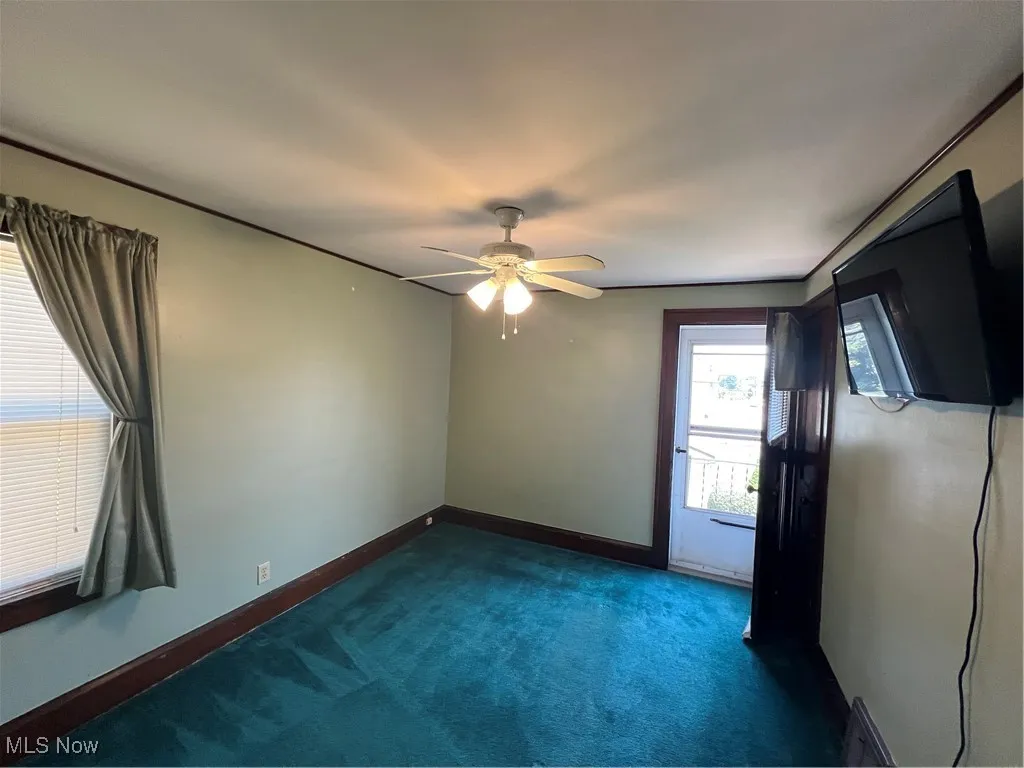 Empty room featuring a ceiling fan and dark colored carpet