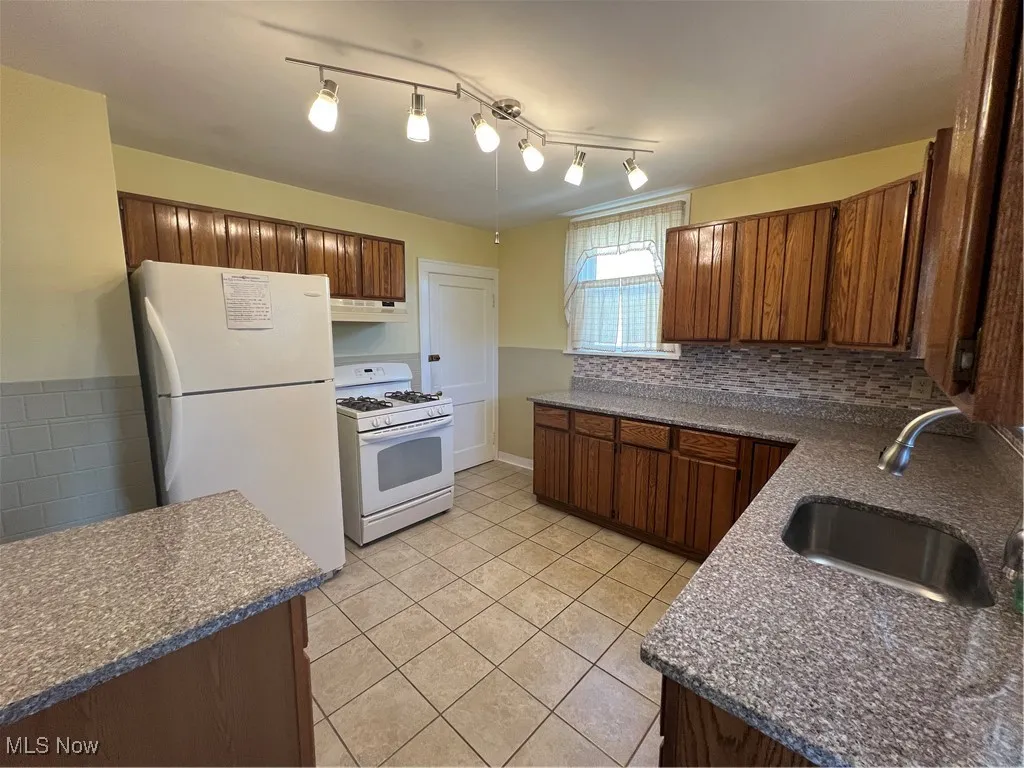 Kitchen with refrigerator, stove, exhaust hood, light tile patterned flooring, and dark countertops