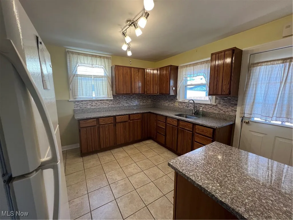 Kitchen with light tile patterned floors, tasteful backsplash, fridge, and dark stone countertops