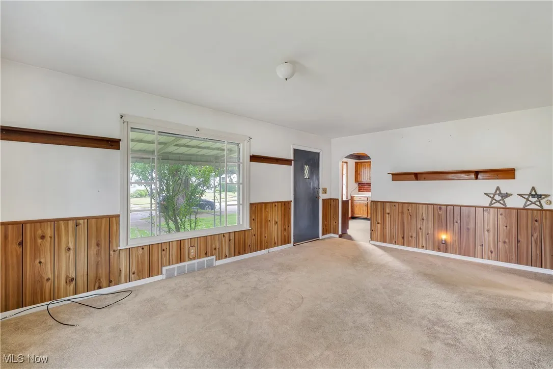 Carpeted spare room featuring arched walkways, wainscoting, and wooden walls
