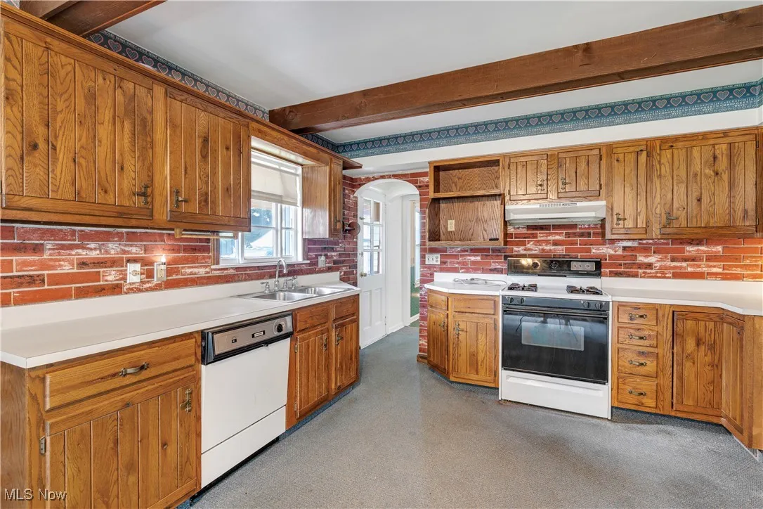 Kitchen featuring white appliances, under cabinet range hood, beamed ceiling, arched walkways, and open shelves