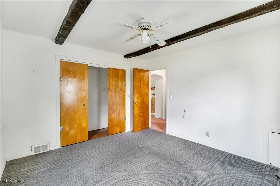Unfurnished bedroom featuring beamed ceiling, carpet floors, arched walkways, a ceiling fan, and a closet