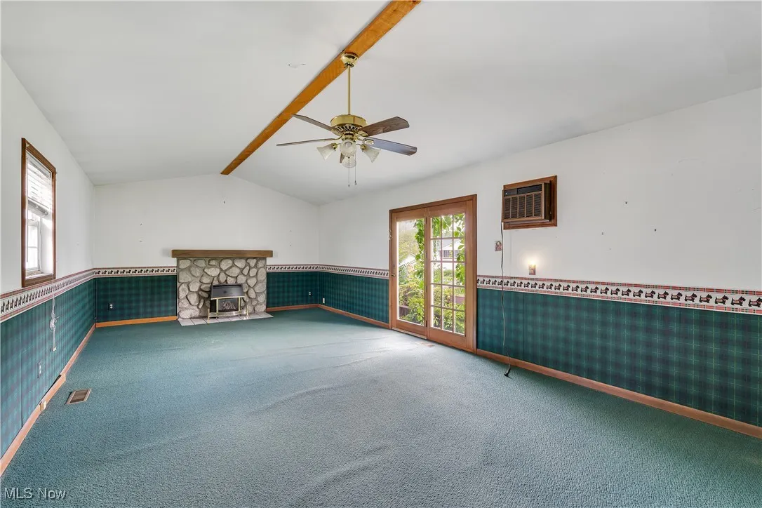 Unfurnished living room featuring a wainscoted wall, a wall mounted air conditioner, ceiling fan, carpet flooring, and a fireplace