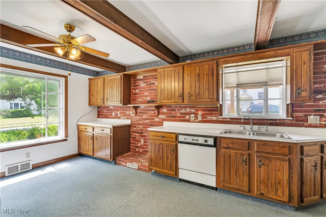 Kitchen featuring dishwasher, light carpet, a ceiling fan, beam ceiling, and brown cabinetry