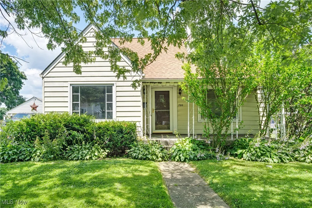 View of front of home with a front yard, roof with shingles, and covered porch
