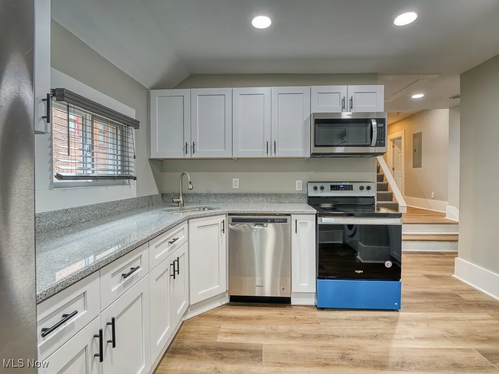 Kitchen featuring stainless steel appliances, light wood-style floors, light stone counters, recessed lighting, and lofted ceiling