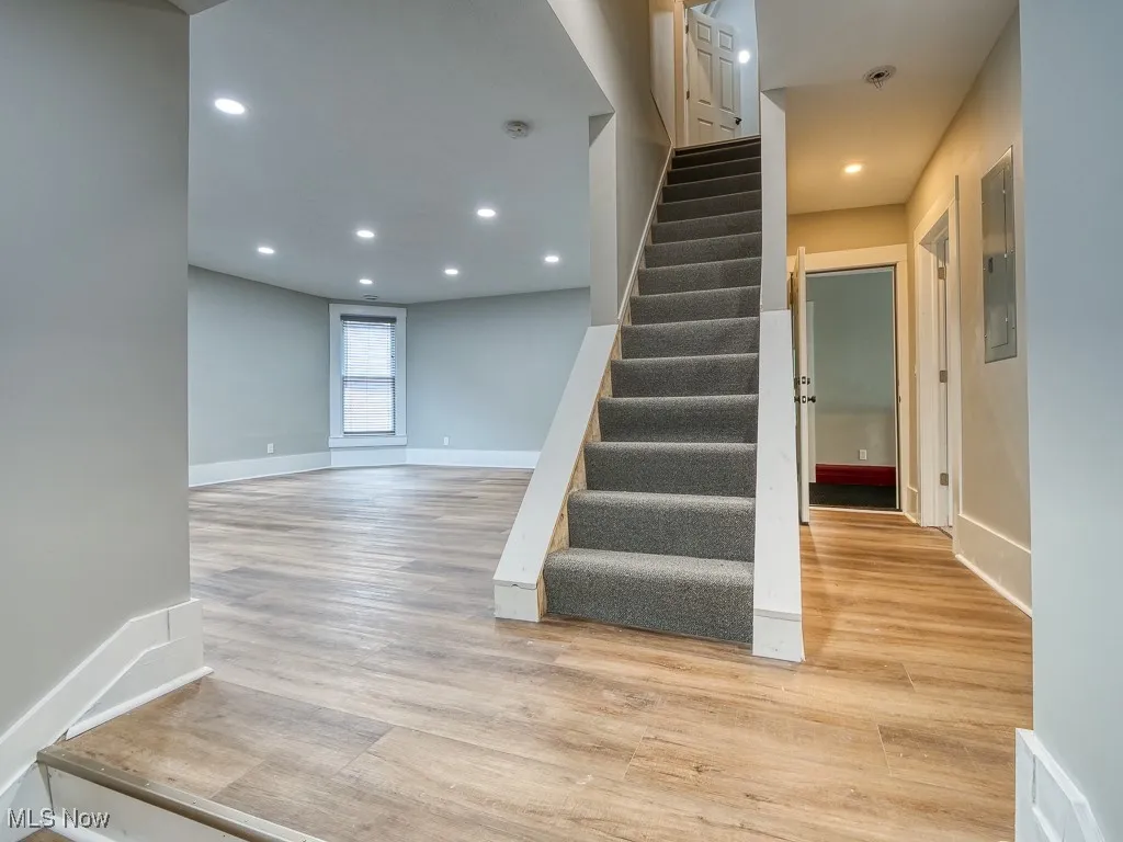 Staircase with wood finished floors, recessed lighting, and electric panel