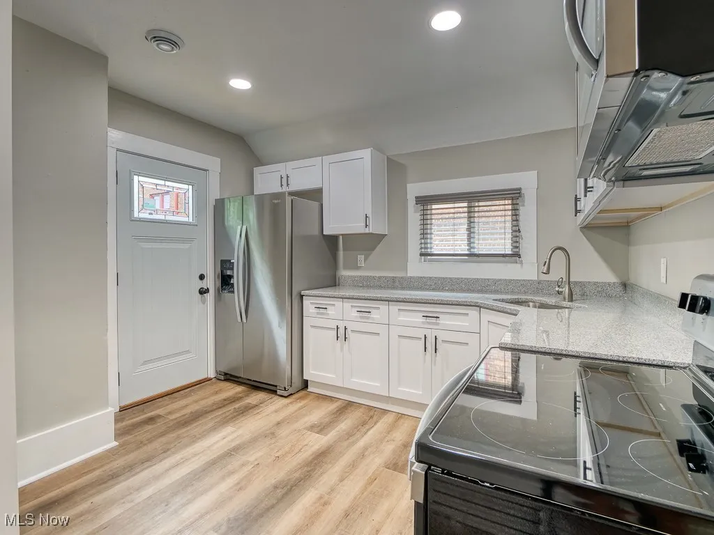Kitchen featuring stainless steel refrigerator with ice dispenser, black electric range, white cabinets, light wood-style flooring, and recessed lighting
