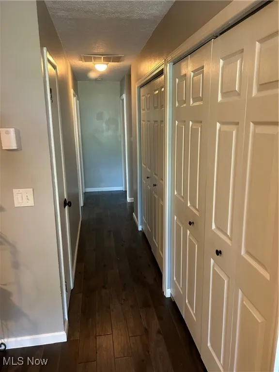 Hallway with a textured ceiling and dark wood finished floors