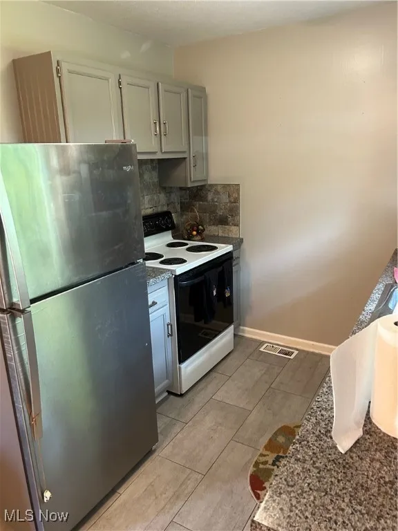 Kitchen featuring refrigerator, range with electric stovetop, decorative backsplash, and light tile patterned flooring