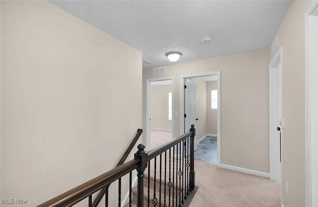 Corridor featuring an upstairs landing, a textured ceiling, and light carpet