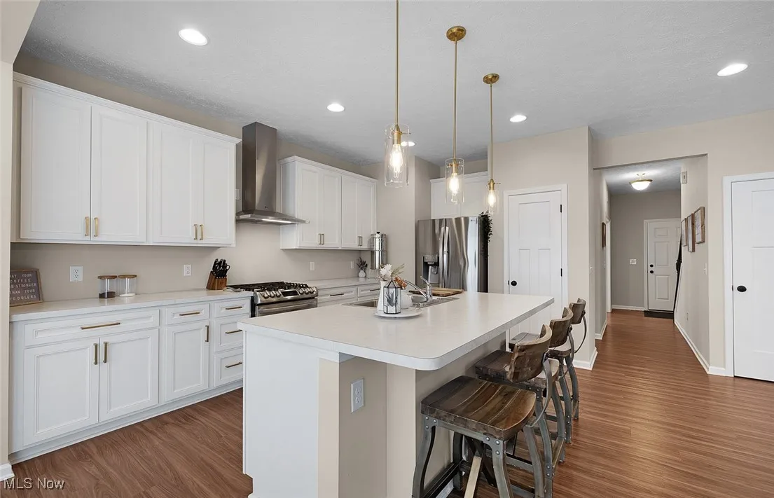 Kitchen featuring wall chimney range hood, stainless steel appliances, wood finished floors, white cabinetry, and light countertops