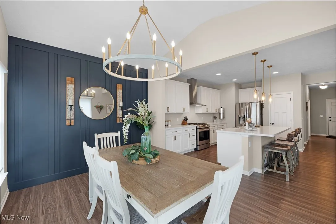 Dining space with dark wood-type flooring, a chandelier, vaulted ceiling, and a decorative wall