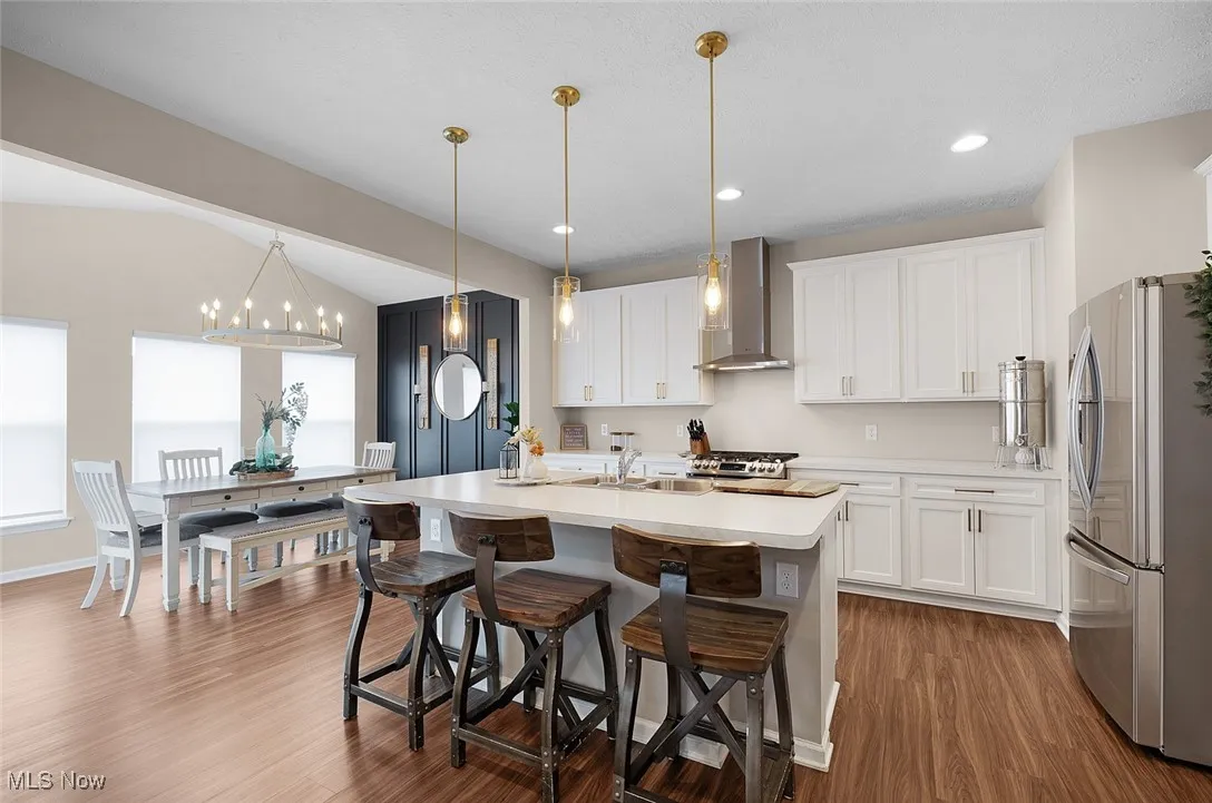 Kitchen with freestanding refrigerator, wall chimney range hood, dark wood finished floors, light countertops, and white cabinetry