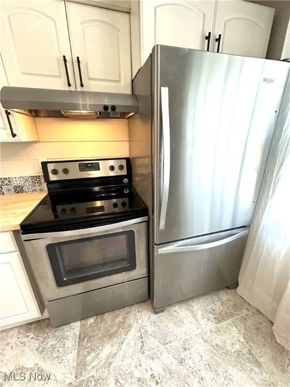 Kitchen featuring stainless steel appliances, under cabinet range hood, white cabinetry, stone finish flooring, and butcher block counters