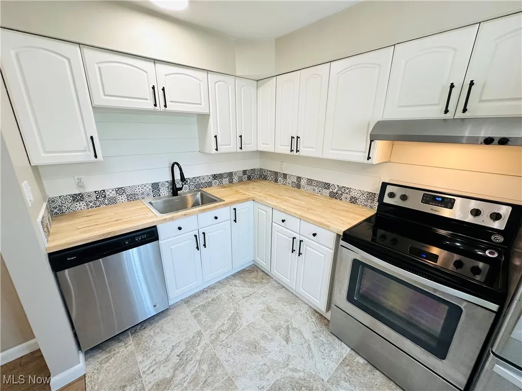 Kitchen featuring stainless steel appliances, under cabinet range hood, butcher block countertops, and white cabinets