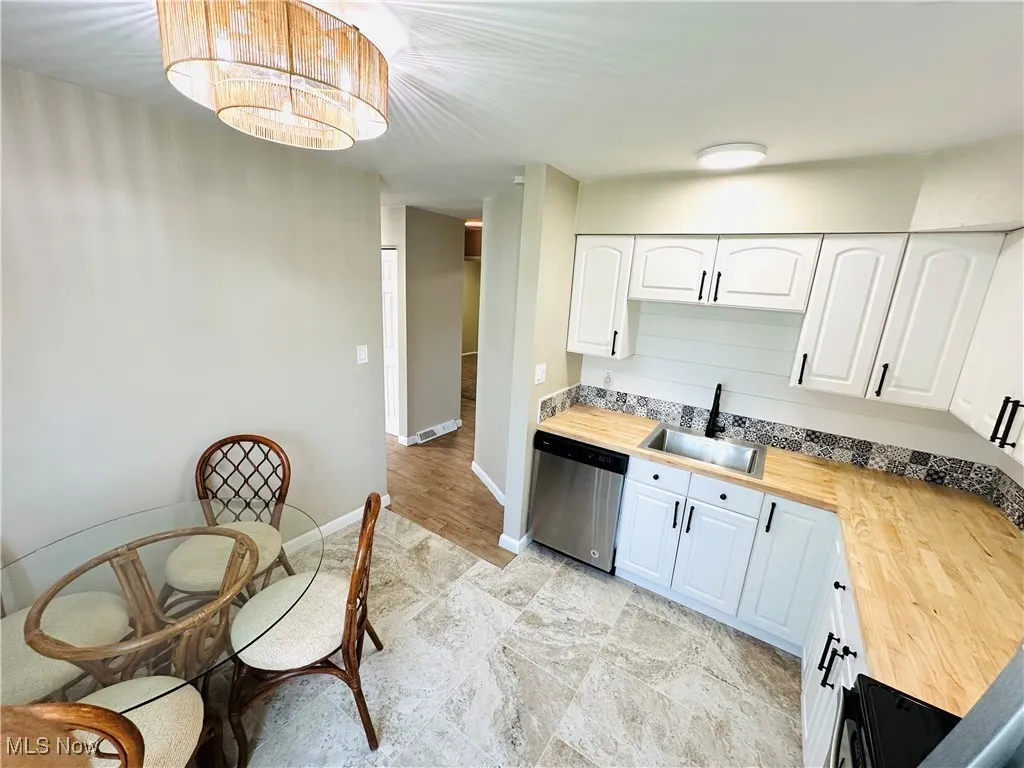Kitchen featuring wooden counters, dishwasher, white cabinets, a chandelier, and decorative light fixtures