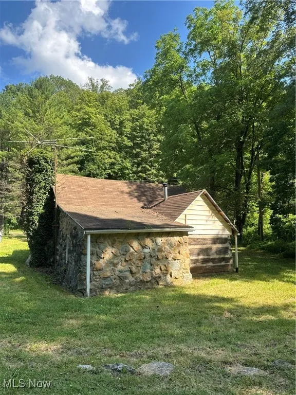 View of property exterior with stone siding, a yard, and a view of trees