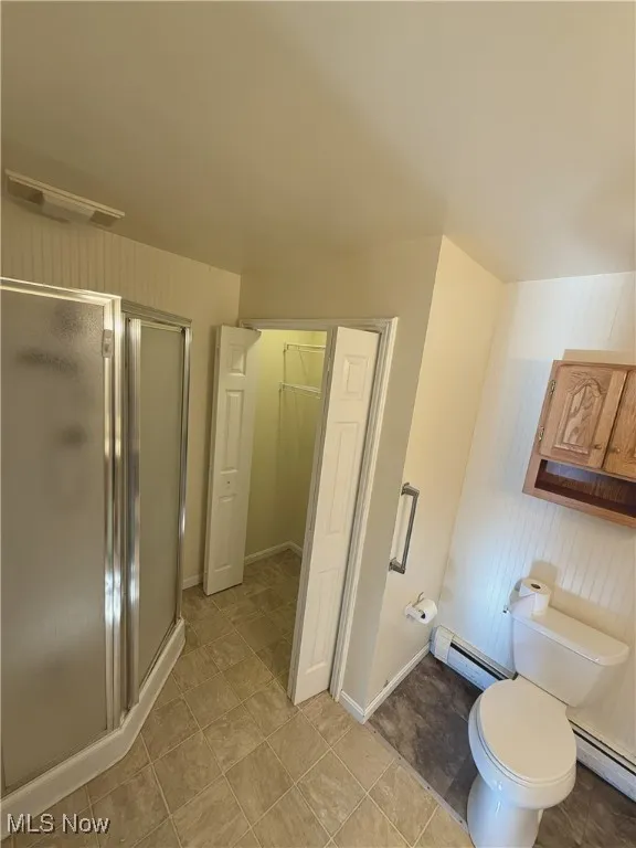 Full bathroom featuring a closet, a stall shower, a baseboard radiator, baseboard heating, and wood walls