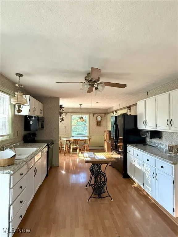 Long, Open Kitchen with wallpapered walls, white cabinets, pendant lighting, light wood-style floors, and black appliances