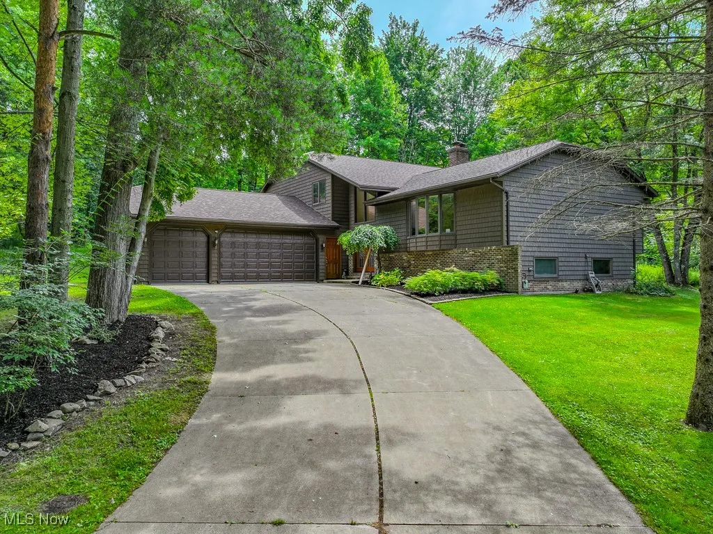 View of front facade with an attached garage, concrete driveway, a chimney, a front lawn, and a shingled roof