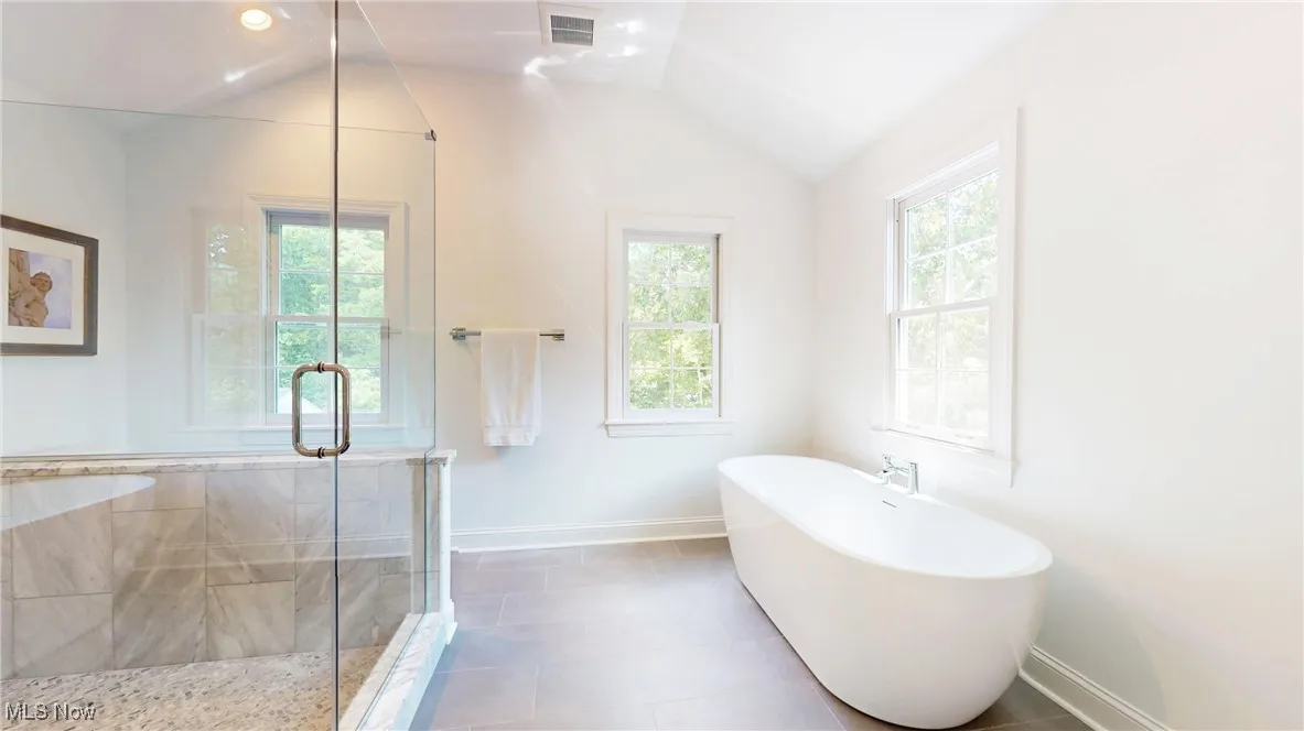 Extra large spa primary bathroom featuring healthy amount of natural light, a freestanding tub, a shower stall, vaulted ceiling, and tile patterned floors