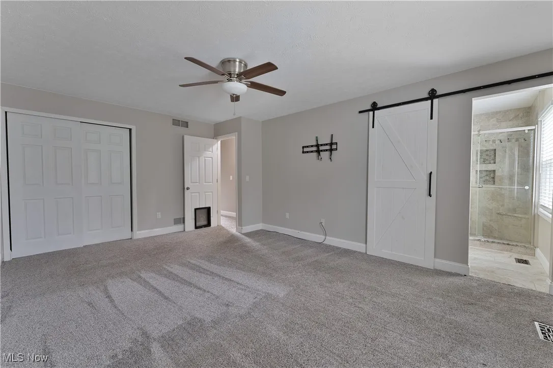 Unfurnished bedroom with carpet floors, a barn door, ceiling fan, connected bathroom, and a closet