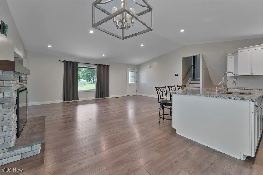 Kitchen with open floor plan, a fireplace, vaulted ceiling, white cabinetry, and light granite countertops