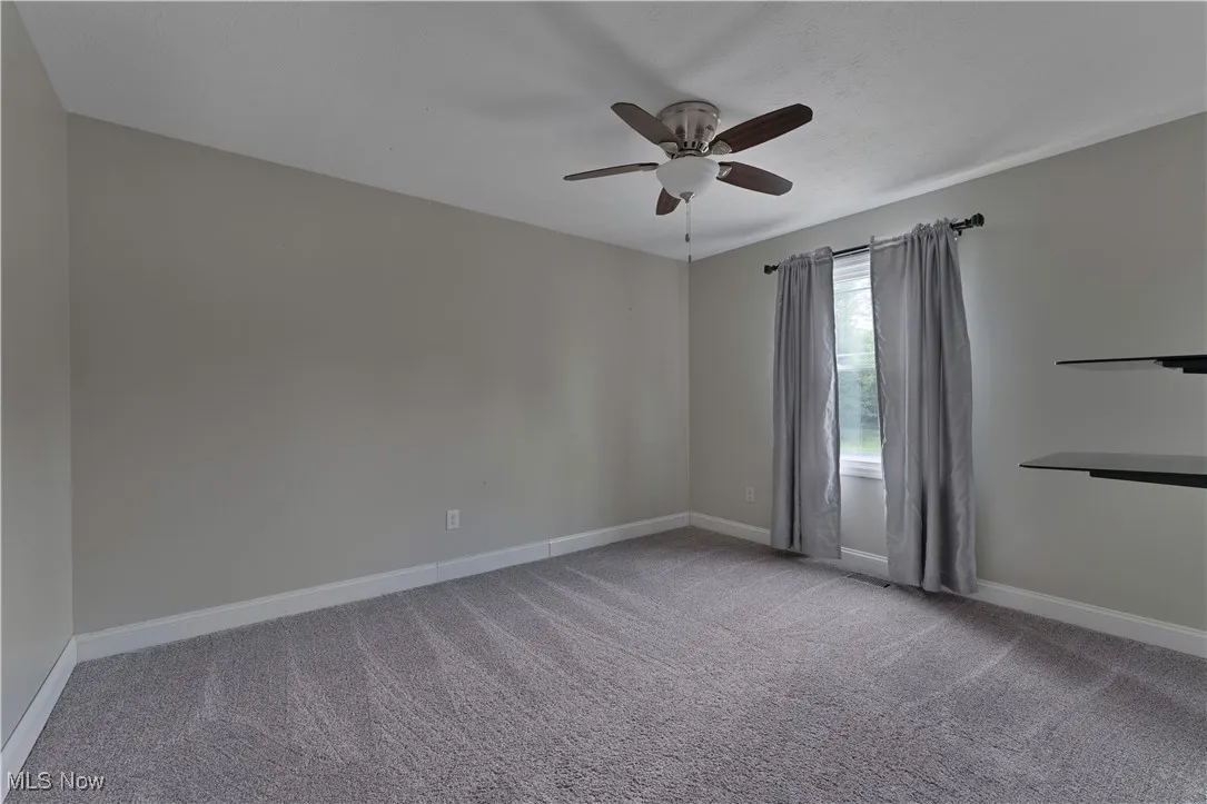 Carpeted empty room with ceiling fan and baseboards